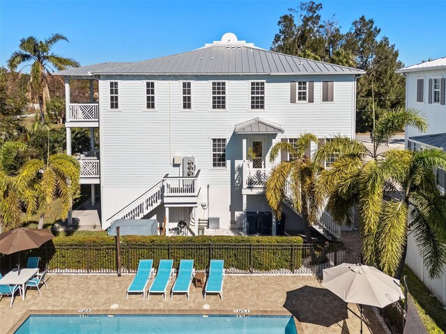 rear view of house with a patio, fence, a community pool, metal roof, and stairs