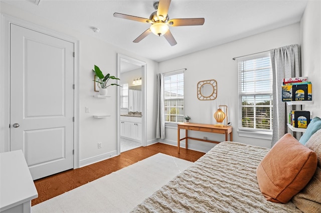 bedroom with multiple windows, ensuite bathroom, baseboards, and wood finished floors