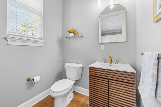 half bathroom with baseboards, toilet, wood finished floors, and vanity