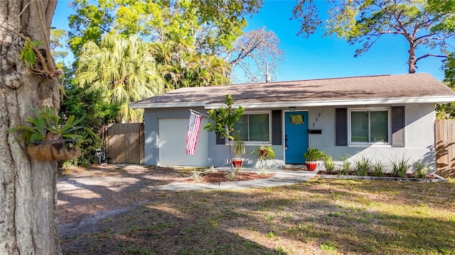 ranch-style house with a front yard, fence, roof with shingles, stucco siding, and a garage