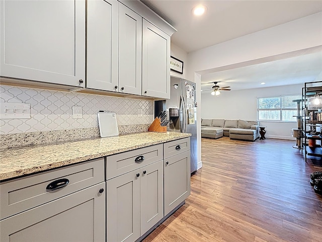 kitchen with a ceiling fan, open floor plan, light wood-style floors, stainless steel fridge with ice dispenser, and decorative backsplash