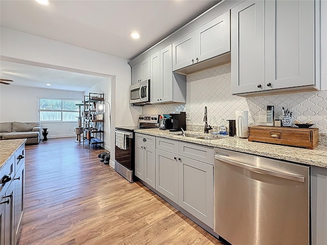 kitchen with open floor plan, stainless steel appliances, light wood-type flooring, and a sink