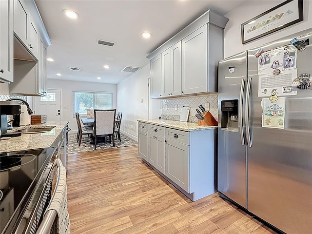 kitchen featuring a sink, light stone countertops, stainless steel refrigerator with ice dispenser, and light wood finished floors