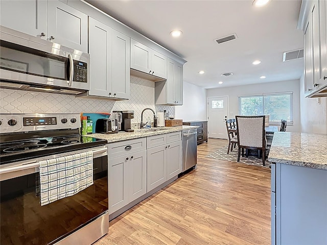 kitchen with light stone countertops, light wood finished floors, a sink, appliances with stainless steel finishes, and tasteful backsplash