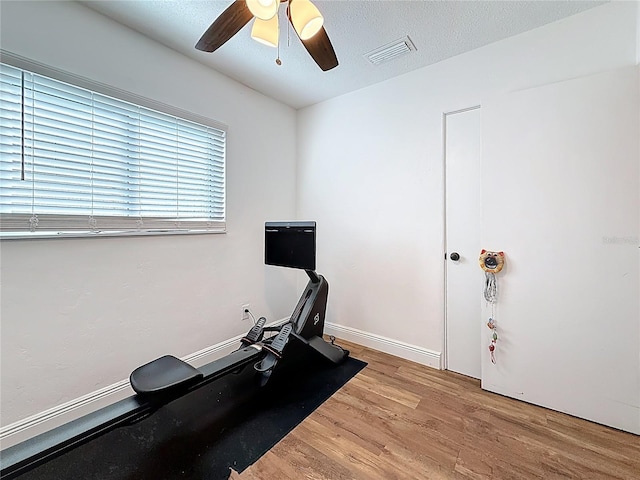 workout room featuring visible vents, a ceiling fan, a textured ceiling, wood finished floors, and baseboards