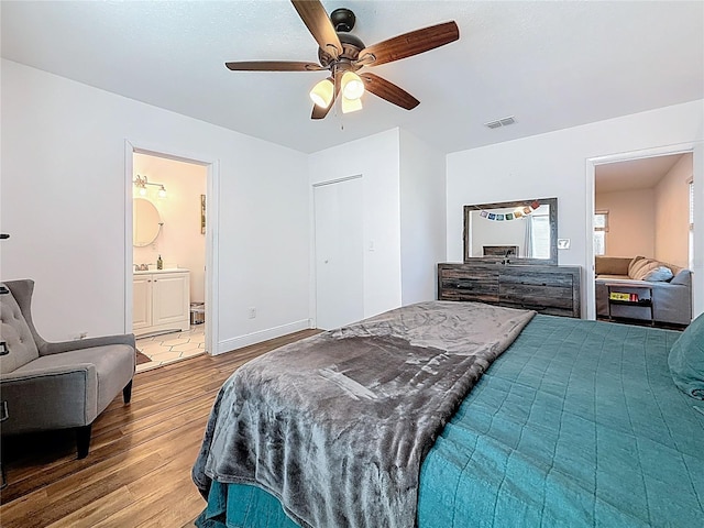 bedroom featuring a ceiling fan, wood finished floors, visible vents, baseboards, and ensuite bath