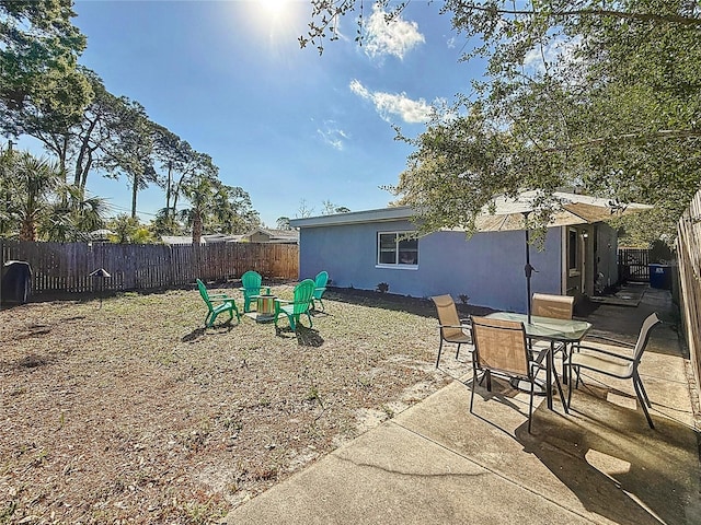 back of property featuring an outdoor fire pit, stucco siding, a fenced backyard, a patio area, and outdoor dining space