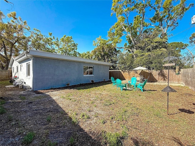 back of house with a fenced backyard, a lawn, and stucco siding