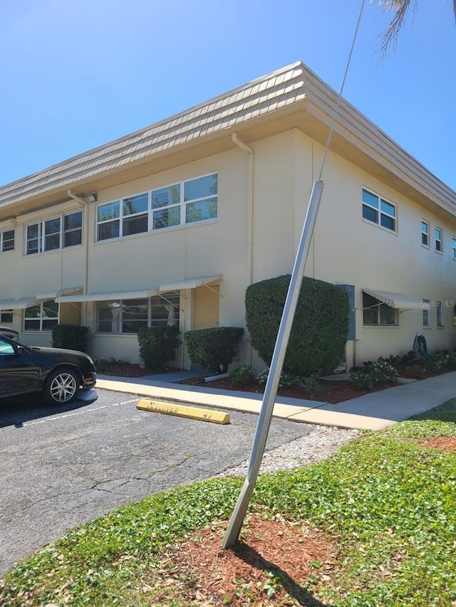 view of side of home with mansard roof, uncovered parking, and stucco siding