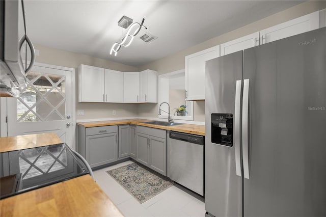 kitchen with visible vents, gray cabinets, a sink, appliances with stainless steel finishes, and wooden counters