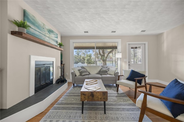 living area featuring a glass covered fireplace, visible vents, a textured ceiling, and wood finished floors