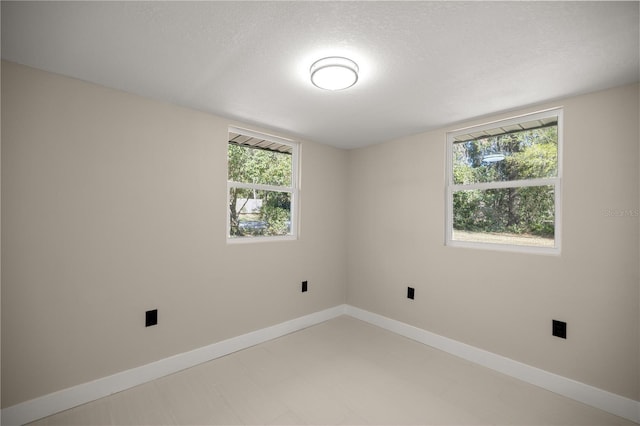 empty room with a wealth of natural light, light floors, a textured ceiling, and baseboards