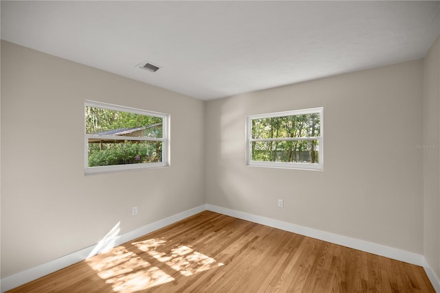 unfurnished room with a wealth of natural light, visible vents, baseboards, and light wood-style floors