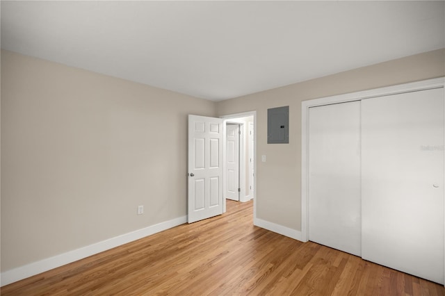 unfurnished bedroom with electric panel, a closet, baseboards, and light wood finished floors