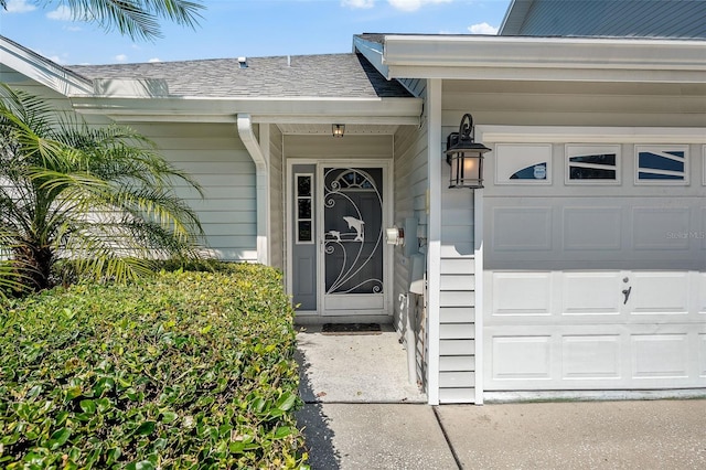 view of exterior entry with an attached garage and a shingled roof