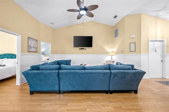 living area with visible vents, a wainscoted wall, lofted ceiling, ceiling fan, and light wood-type flooring