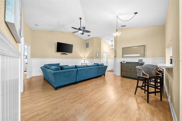 living area featuring a wainscoted wall, light wood-style floors, a ceiling fan, and vaulted ceiling