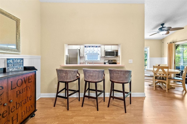 kitchen with a wainscoted wall, a kitchen breakfast bar, appliances with stainless steel finishes, and wood finished floors