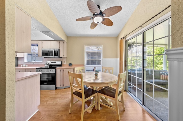 dining area featuring a wainscoted wall, light wood-style flooring, a textured ceiling, and ceiling fan