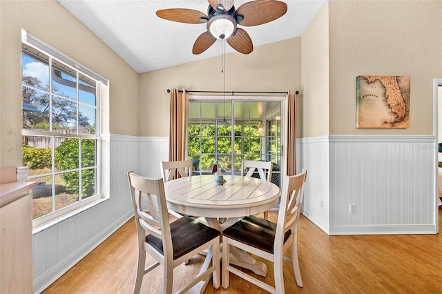 dining area featuring light wood-type flooring, ceiling fan, wainscoting, and vaulted ceiling