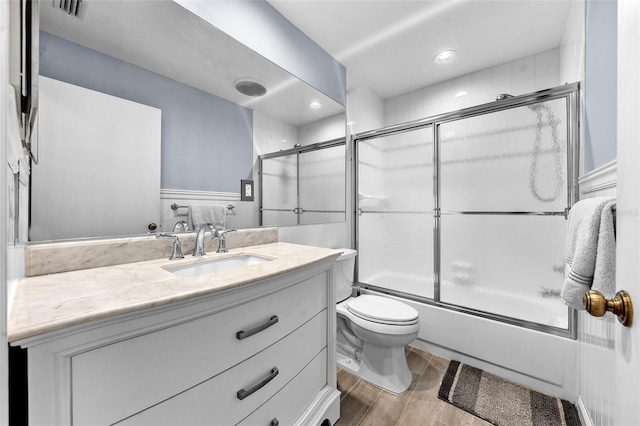 full bath featuring visible vents, toilet, wood finished floors, shower / bath combination with glass door, and vanity