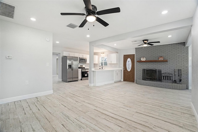 unfurnished living room with light wood finished floors, visible vents, a fireplace, and baseboards