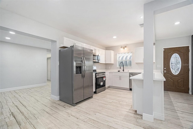 kitchen featuring a peninsula, stainless steel appliances, light countertops, white cabinets, and light wood-type flooring