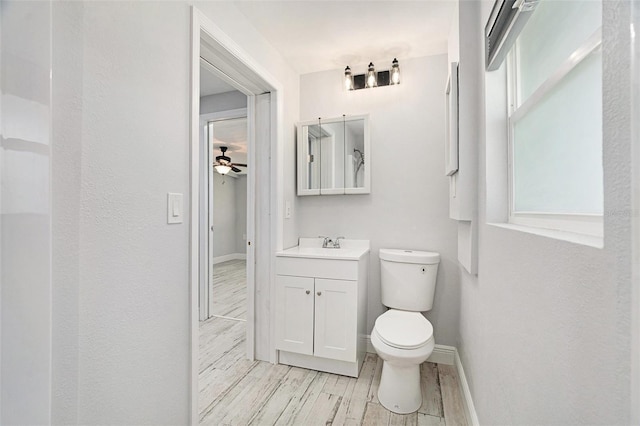 bathroom featuring baseboards, wood finish floors, toilet, vanity, and a ceiling fan