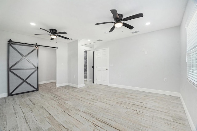 spare room featuring a barn door, baseboards, visible vents, and light wood finished floors