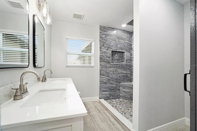 bathroom featuring visible vents, a sink, wood finished floors, baseboards, and tiled shower