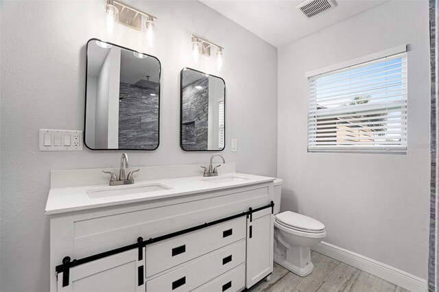 bathroom with visible vents, toilet, wood finished floors, and a sink