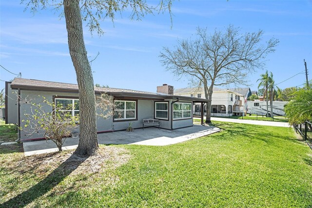 back of house featuring stucco siding, a lawn, a chimney, a sunroom, and a patio area