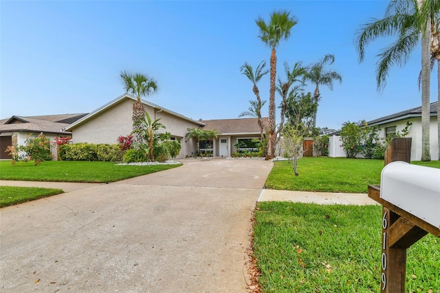 view of front facade with stucco siding, driveway, a front yard, and fence