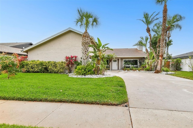 mid-century home with stucco siding, a front yard, driveway, and fence