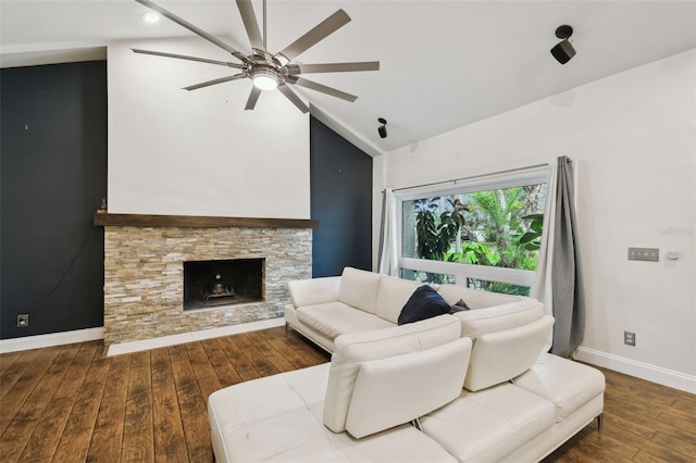 living area with hardwood / wood-style floors, a ceiling fan, baseboards, a stone fireplace, and vaulted ceiling