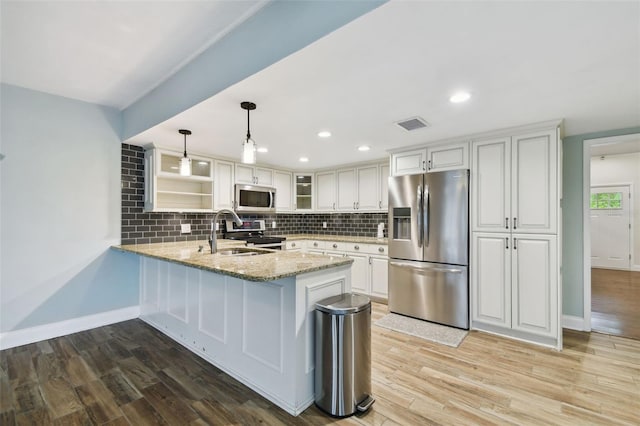 kitchen with a peninsula, light wood-style floors, backsplash, and stainless steel appliances