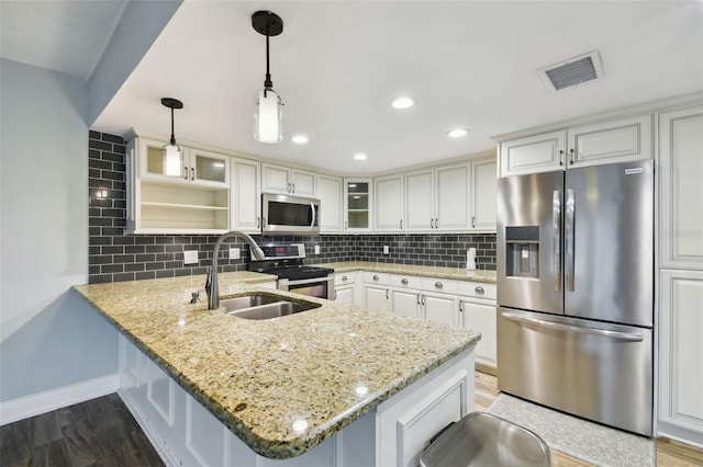 kitchen featuring visible vents, a peninsula, a sink, appliances with stainless steel finishes, and tasteful backsplash