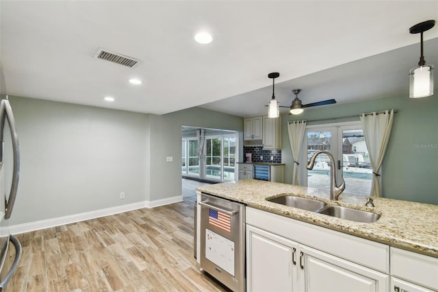 kitchen with tasteful backsplash, visible vents, light wood-style flooring, hanging light fixtures, and a sink