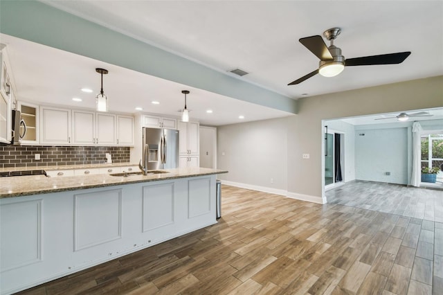 kitchen featuring visible vents, stainless steel refrigerator with ice dispenser, backsplash, white cabinets, and light stone countertops