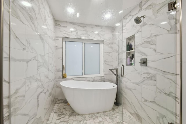 bathroom with a marble finish shower, stone wall, a freestanding bath, and tile walls