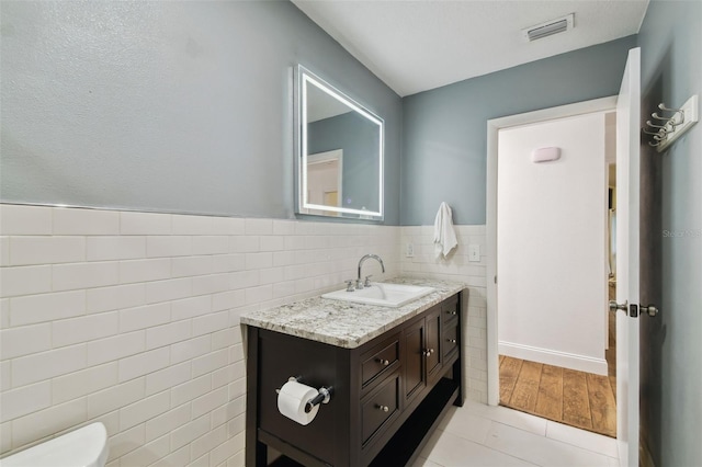 half bath featuring visible vents, a wainscoted wall, toilet, tile walls, and vanity