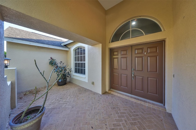 view of exterior entry featuring stucco siding and a shingled roof