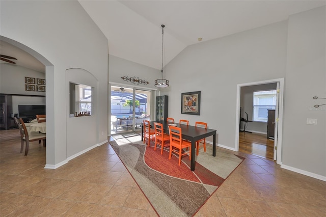 dining area with light tile patterned floors, arched walkways, high vaulted ceiling, and a ceiling fan