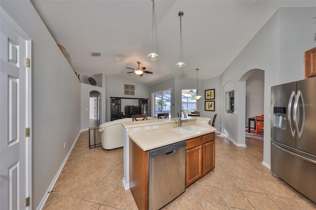 kitchen with arched walkways, appliances with stainless steel finishes, brown cabinetry, and a sink