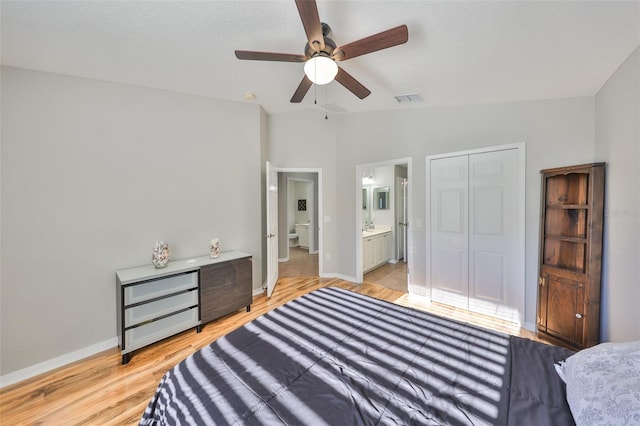 bedroom featuring light wood finished floors, visible vents, baseboards, lofted ceiling, and ensuite bath