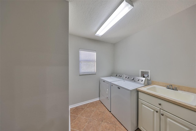 clothes washing area featuring a sink, a textured ceiling, washing machine and dryer, cabinet space, and light tile patterned flooring