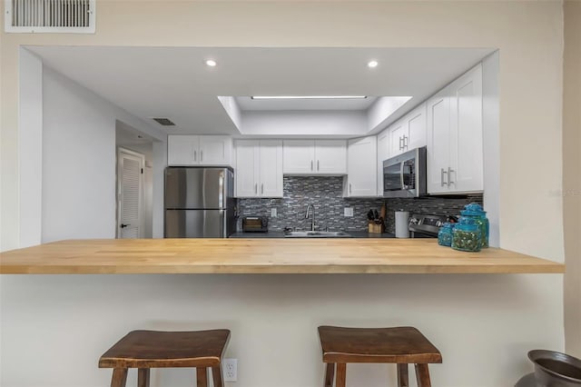 kitchen with visible vents, a sink, stainless steel appliances, wood counters, and tasteful backsplash