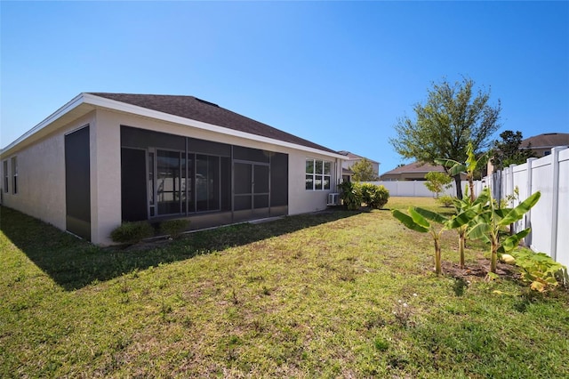 back of property with a yard, a sunroom, a fenced backyard, and stucco siding