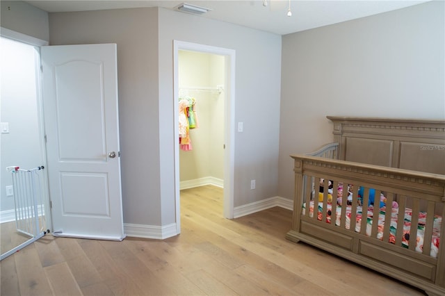 bedroom featuring a spacious closet, light wood-style floors, visible vents, and baseboards