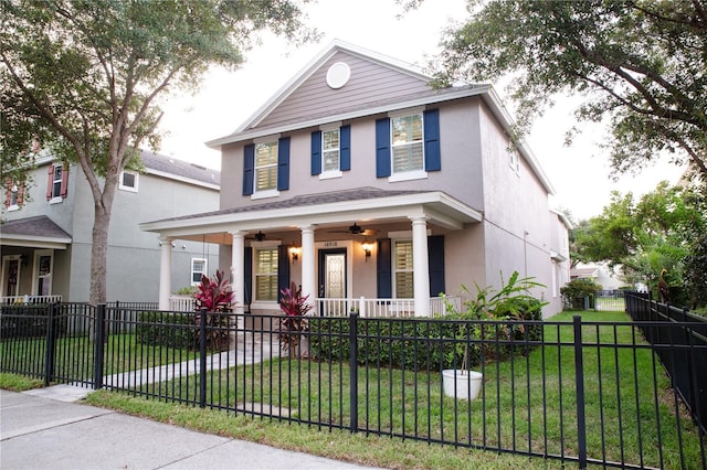 view of front of property featuring a ceiling fan, covered porch, stucco siding, a front lawn, and a fenced front yard